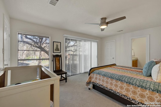 carpeted bedroom with ensuite bath, visible vents, and a ceiling fan