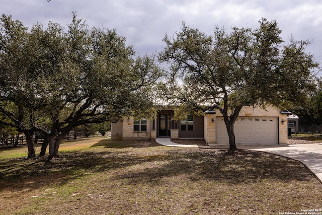 view of property hidden behind natural elements with an attached garage, stone siding, and concrete driveway