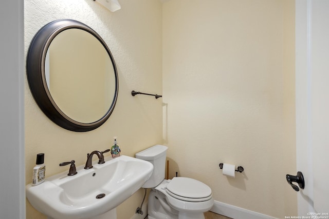 half bathroom with baseboards, a sink, and toilet