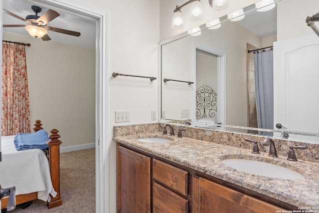 ensuite bathroom featuring double vanity, a sink, a ceiling fan, and baseboards