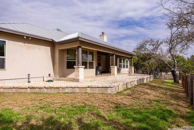 back of house with metal roof, fence, a lawn, stucco siding, and a standing seam roof