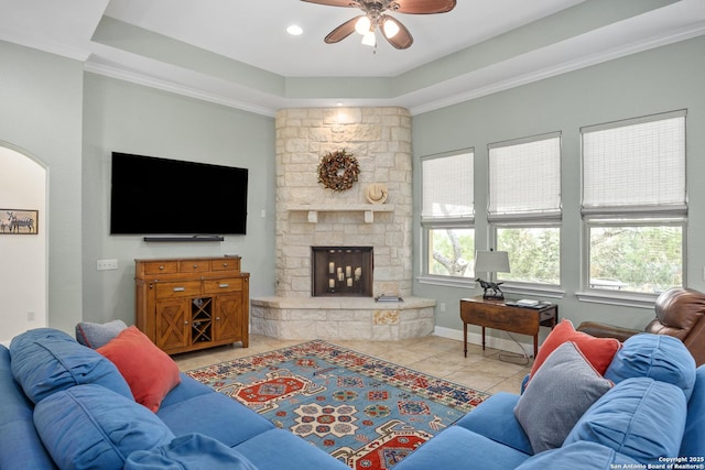 tiled living room with a healthy amount of sunlight, arched walkways, a raised ceiling, and a stone fireplace