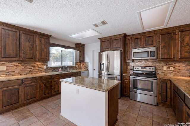 kitchen featuring light tile patterned flooring, a kitchen island, a sink, visible vents, and appliances with stainless steel finishes