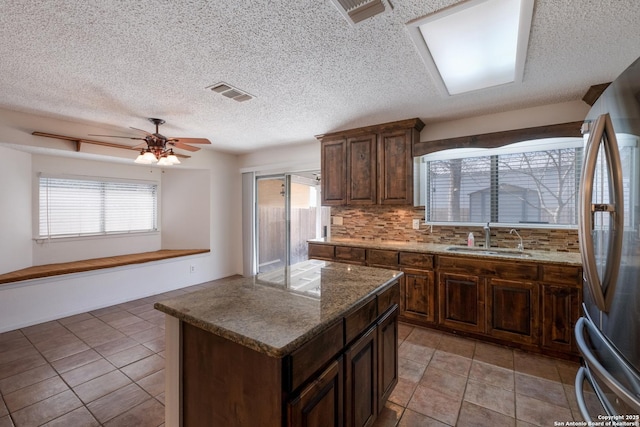 kitchen with freestanding refrigerator, visible vents, a sink, and decorative backsplash