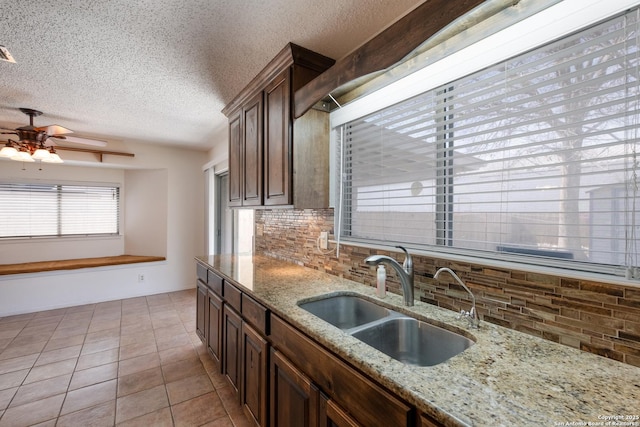 kitchen with a textured ceiling, ceiling fan, light tile patterned flooring, a sink, and decorative backsplash