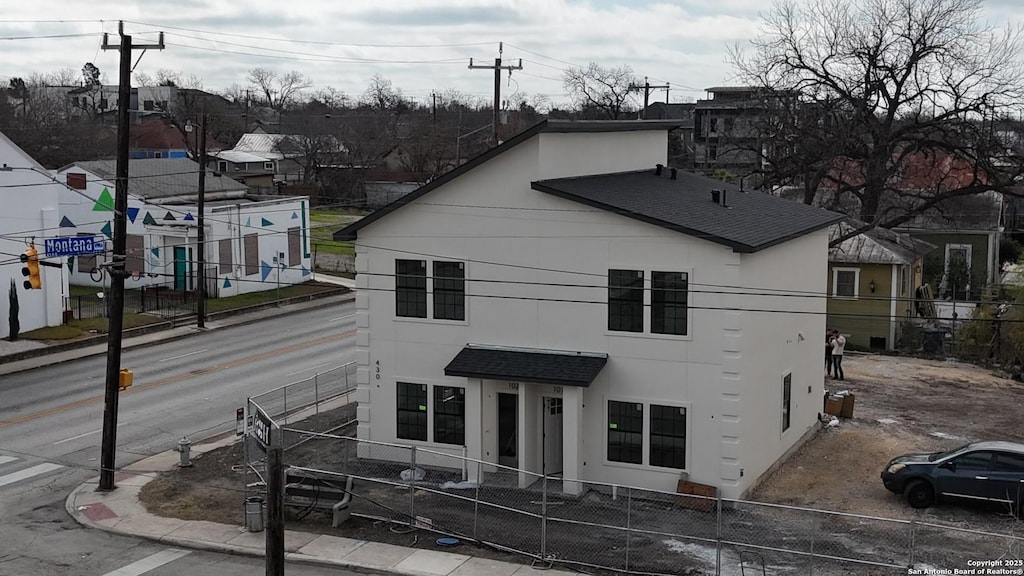 view of front facade featuring a shingled roof, fence private yard, and stucco siding