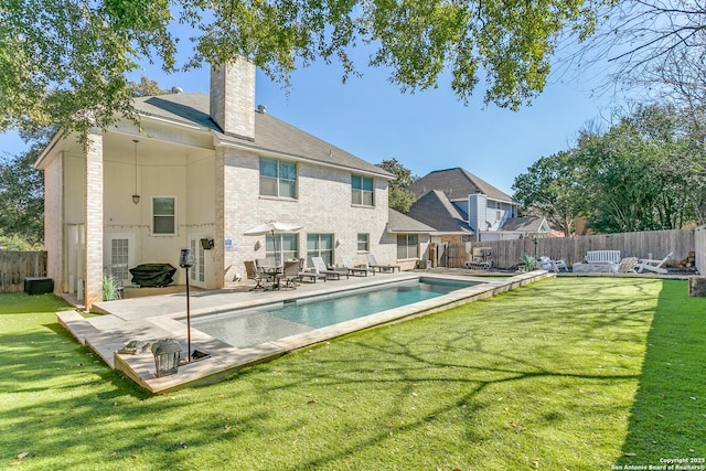 rear view of house featuring a patio area, a fenced backyard, a chimney, and a yard