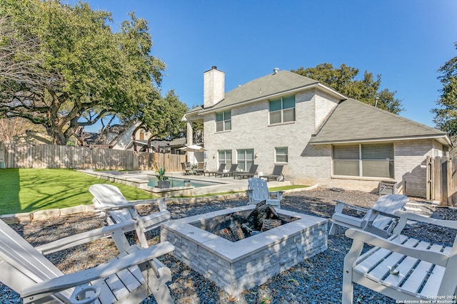 rear view of house with a patio, a fenced backyard, a fire pit, brick siding, and a chimney