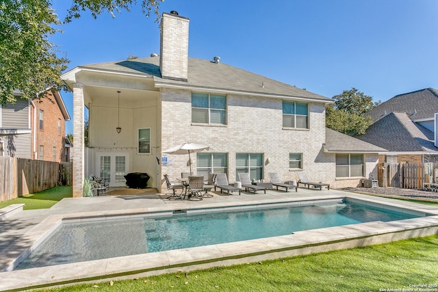 rear view of property featuring a fenced in pool, brick siding, a chimney, a patio area, and a fenced backyard