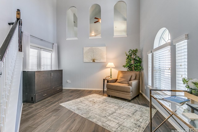 sitting room with ceiling fan, a towering ceiling, baseboards, and wood finished floors