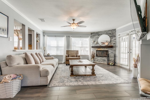 living room with a stone fireplace, plenty of natural light, wood finished floors, and visible vents