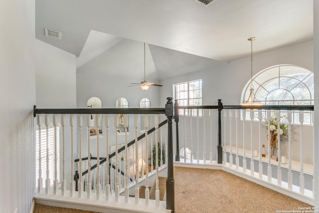 hallway with carpet floors, lofted ceiling, visible vents, and an upstairs landing