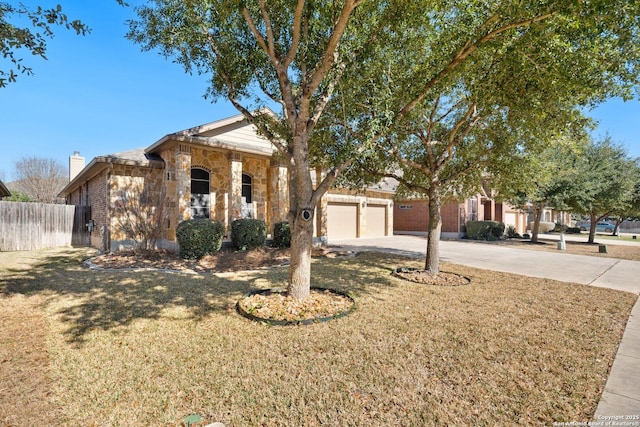 view of front of property with an attached garage, fence, stone siding, concrete driveway, and a front yard