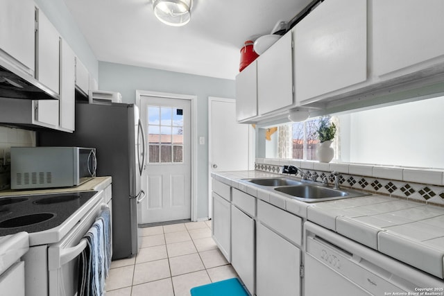 kitchen featuring light tile patterned floors, backsplash, white cabinets, a sink, and white appliances