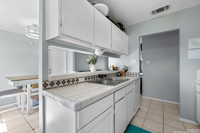 kitchen featuring tile countertops, visible vents, white cabinets, and a sink