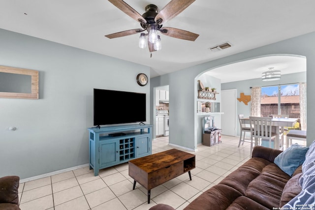 living area featuring arched walkways, light tile patterned floors, visible vents, ceiling fan, and baseboards