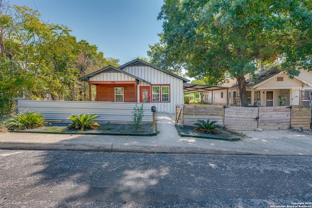 bungalow with board and batten siding, a fenced front yard, and a carport