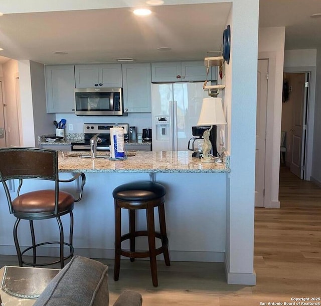 kitchen featuring light wood-style flooring, stainless steel appliances, a peninsula, a kitchen breakfast bar, and light stone countertops