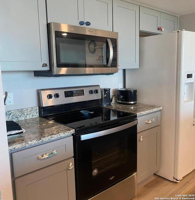 kitchen featuring stainless steel appliances, gray cabinetry, light wood finished floors, and light stone countertops