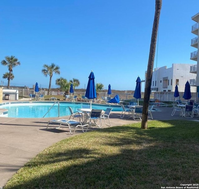 community pool featuring a patio area, fence, and a lawn