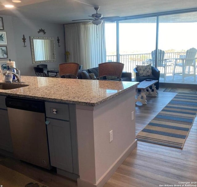 kitchen with a sink, light wood-style flooring, light stone counters, and dishwasher