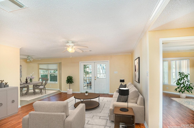 living area with crown molding, visible vents, plenty of natural light, and wood finished floors