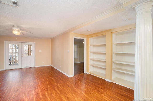 spare room featuring built in features, visible vents, wood finished floors, a textured ceiling, and ornate columns