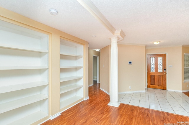 foyer entrance featuring ornate columns, baseboards, a textured ceiling, and wood finished floors