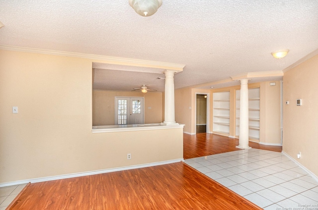 empty room with a textured ceiling, wood finished floors, a ceiling fan, ornate columns, and crown molding