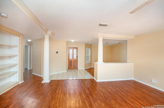 entrance foyer featuring ornate columns, visible vents, wood finished floors, and ornamental molding