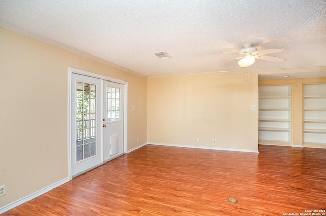 empty room with built in features, crown molding, a textured ceiling, light wood-type flooring, and baseboards