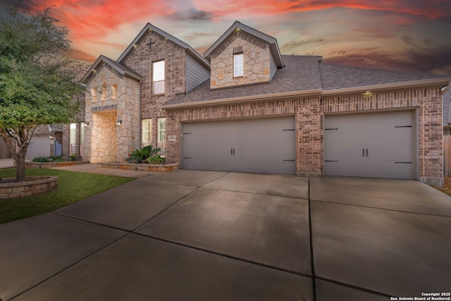 view of front facade featuring an attached garage, brick siding, driveway, stone siding, and roof with shingles