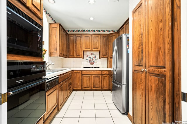 kitchen featuring light tile patterned flooring, a sink, light countertops, black appliances, and brown cabinetry