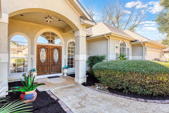 entrance to property featuring roof with shingles, an attached garage, and stucco siding