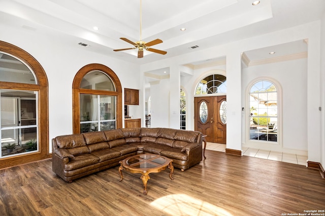 living room with light wood-type flooring, a raised ceiling, visible vents, and baseboards