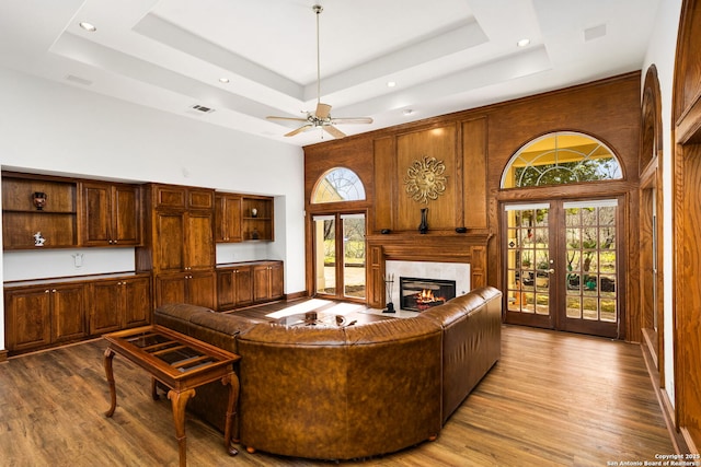 living room with a raised ceiling, a glass covered fireplace, wood finished floors, a high ceiling, and french doors