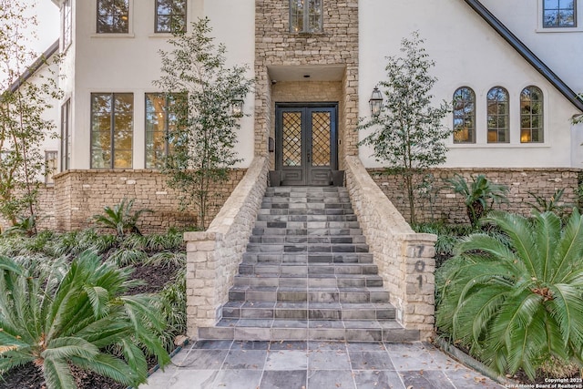 doorway to property with stucco siding, stone siding, and french doors