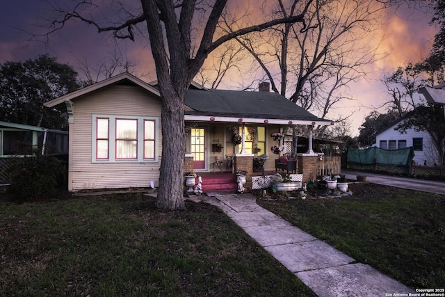 view of front of property with covered porch, a lawn, and a chimney