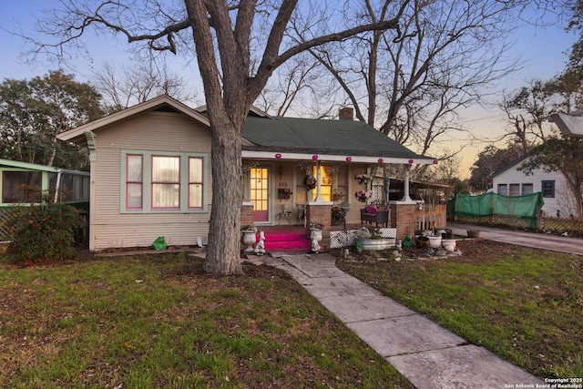 view of front of house with covered porch, a lawn, and a chimney