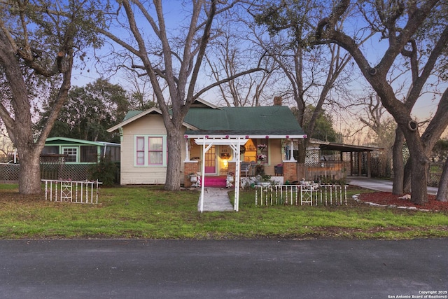 view of front of property with a chimney, covered porch, fence, a front lawn, and a carport