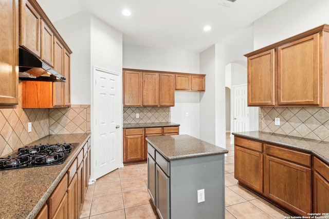 kitchen featuring light tile patterned floors, arched walkways, brown cabinetry, black gas cooktop, and under cabinet range hood