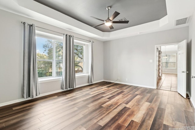 empty room featuring a raised ceiling, visible vents, ceiling fan, wood finished floors, and baseboards