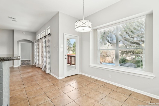 unfurnished dining area featuring light tile patterned floors, baseboards, visible vents, and arched walkways