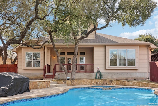 back of property with an in ground hot tub, roof with shingles, fence, and an outdoor pool