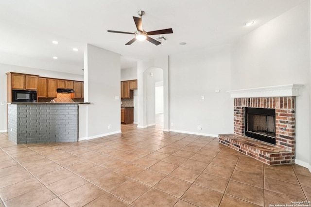 unfurnished living room featuring a ceiling fan, a brick fireplace, baseboards, and light tile patterned floors