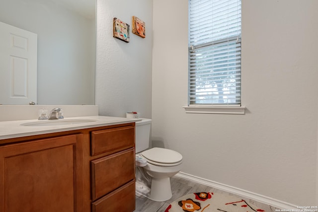 bathroom with toilet, baseboards, wood finished floors, and vanity