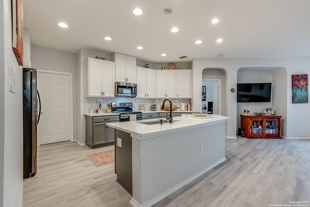 kitchen with arched walkways, a sink, appliances with stainless steel finishes, light wood-type flooring, and backsplash