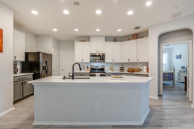 kitchen featuring stainless steel appliances, a sink, light countertops, tasteful backsplash, and an island with sink