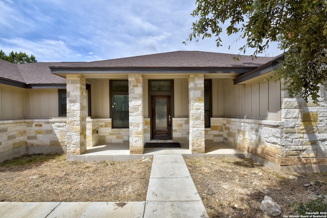 view of front of property featuring covered porch, stone siding, a shingled roof, and board and batten siding