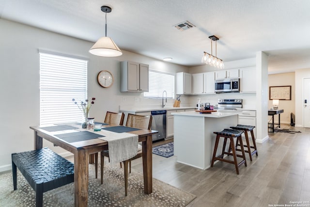 kitchen featuring visible vents, light wood-style flooring, appliances with stainless steel finishes, a center island, and a kitchen bar